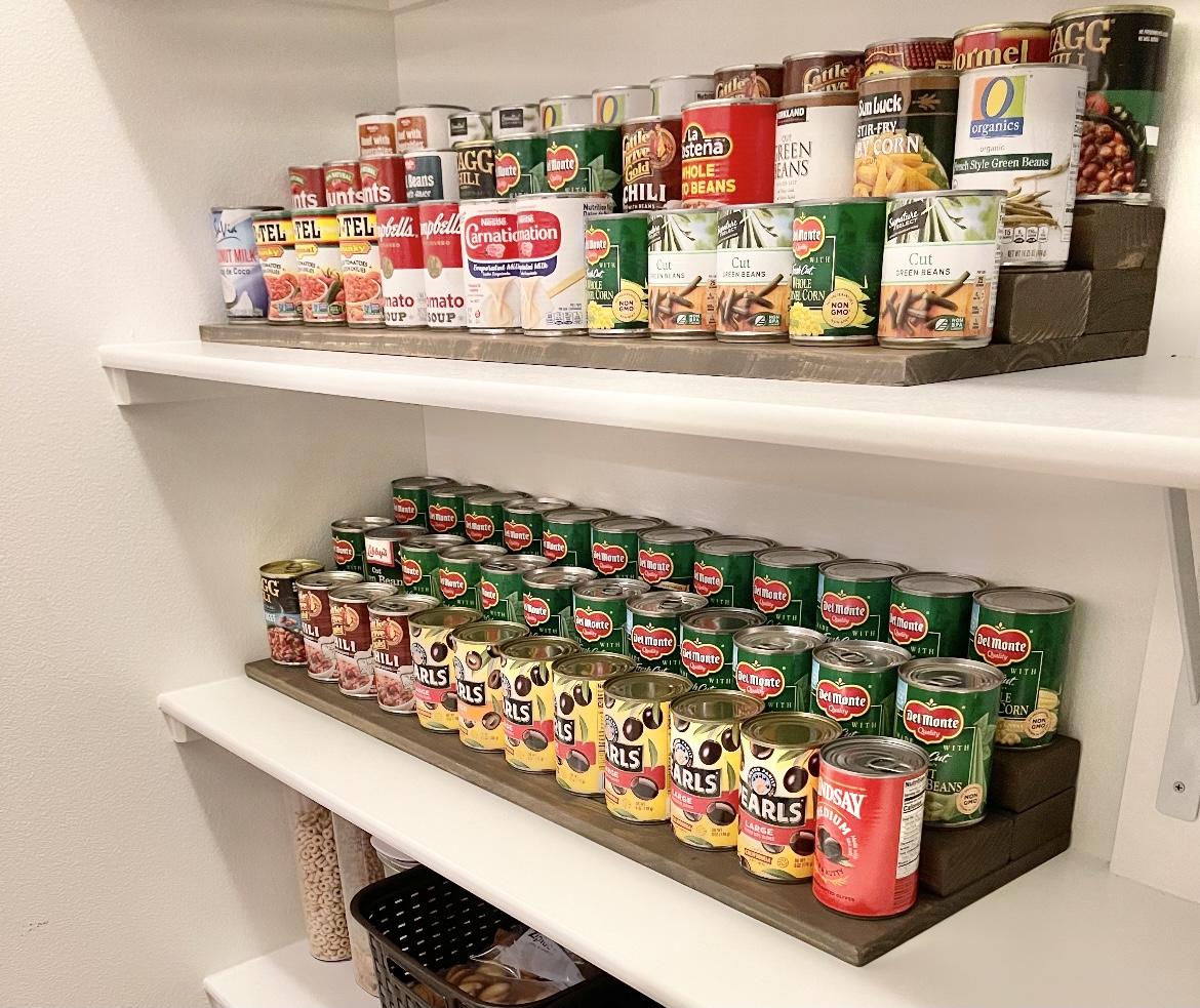 Wooden tiered can risers improve visibility across rows of canned pantry staples.