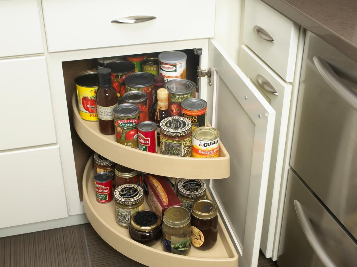 Rotating lazy Susan shelves organize canned goods and jars inside a corner kitchen cabinet.